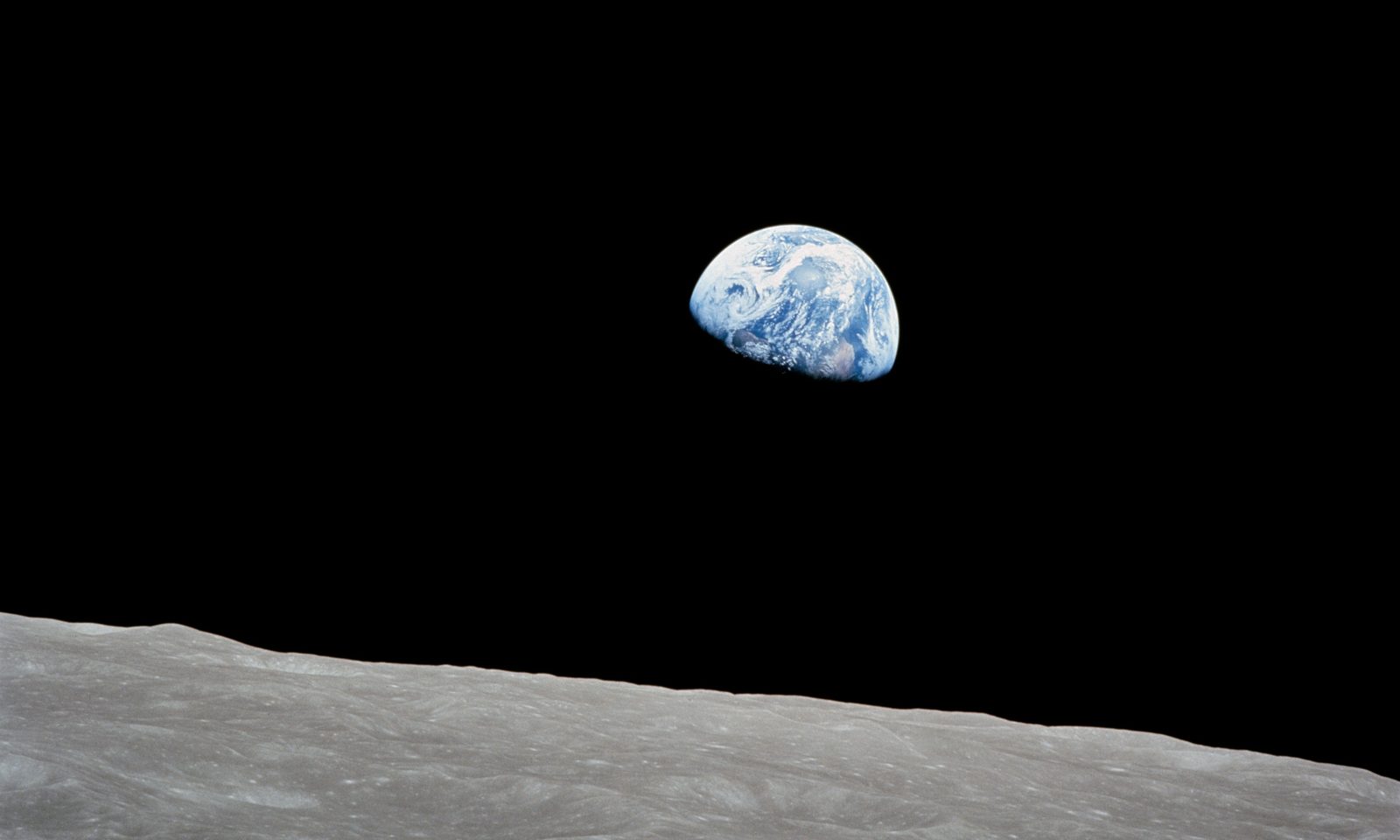 Earth rising above the barren lunar horizon, photographed from lunar orbit against black space.